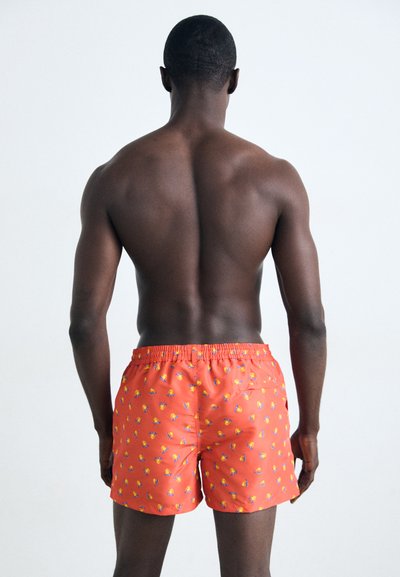 Lys orange svømmeshorts med et morsomt mønster av små fargerike frukter, elastisk midje og en baklomme. Materialet virker lett.
