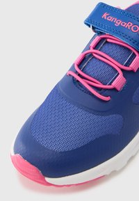 Μπλε αθλητικό παπούτσι με επάνω μέρος από υφή πλέγματος, ροζ λεπτομέρειες και λουράκι με αυτοκόλλητο. Διαθέτει στρογγυλεμένη μύτη και αντίθετη ροζ εξωτερική σόλα.