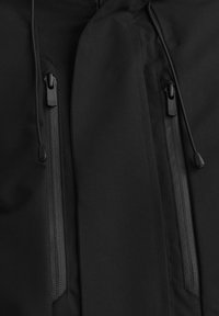 Svart jacktyg med slät yta, med två fickor med dragkedja och justerbara dragsnören vid halslinningen. Minimalistisk design.