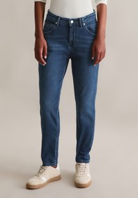 Denim jeans in een medium blauwe wassing, met een smalle taille, rechte pijpen en een klassiek vijf-pocket ontwerp. Gecombineerd met beige sneakers.