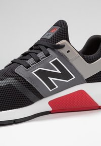 Černošedá sportovní obuv s prodyšným svrškem z mesh materiálu, gumovou podrážkou, výrazným bílým logem "N" a červenými akcenty na patě.