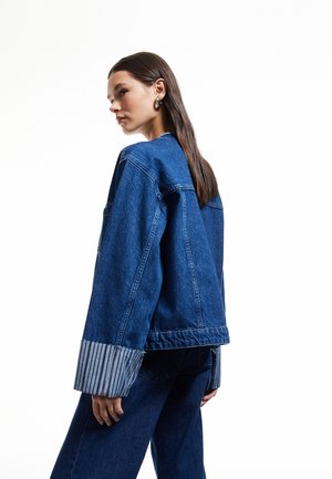 Jeansjacke mit dunkler Wäsche, oversized Design und gestreiften Stoffmanschetten. Keine sichtbaren Verschlüsse oder Verzierungen.