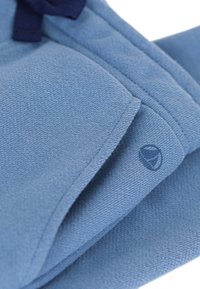 Pullover aus lichtblauem Stoff mit glatter Textur, dunkelblauem Kordelzug und kleinem Logo-Akzent. Klassisches Rundhals-Design.