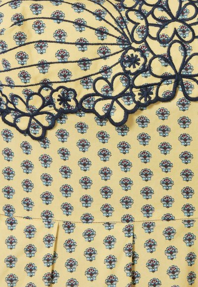 Vestito di cotone con sfondo giallo, caratterizzato da un motivo floreale in blu e rosso. Accenti in pizzo ricamato blu scuro nella parte superiore.