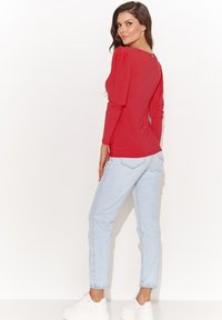 Czerwona bluzka z długim rękawem, z bufkami, z wycięciem na plecach; połączona z jasnoniebieskimi dżinsami i białymi trampkami na platformie. Gładka faktura, dopasowany krój.