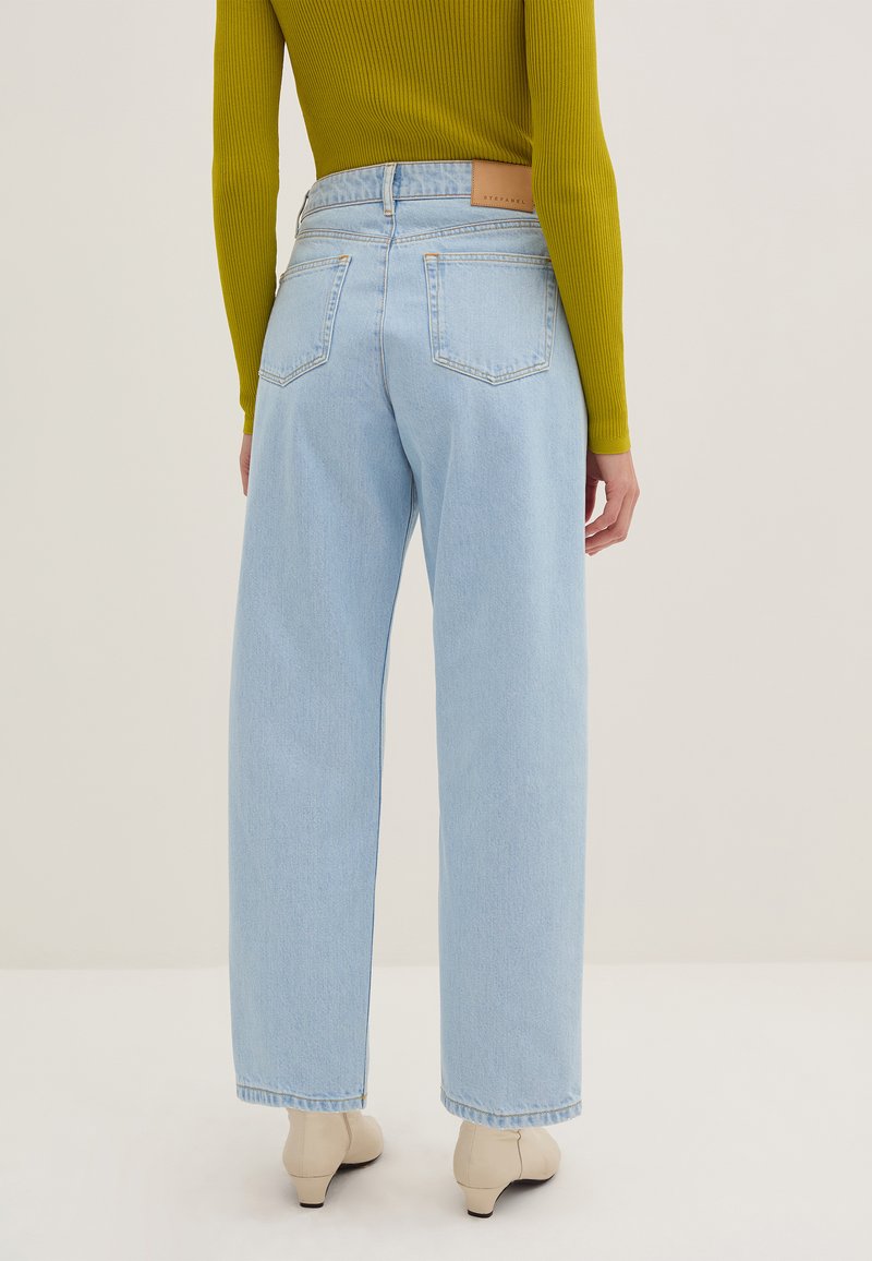 Jeans a vita alta di colore blu chiaro con gamba larga, dotati di una patch in pelle sulla vita posteriore, due tasche posteriori e un orlo leggermente sfilacciato.