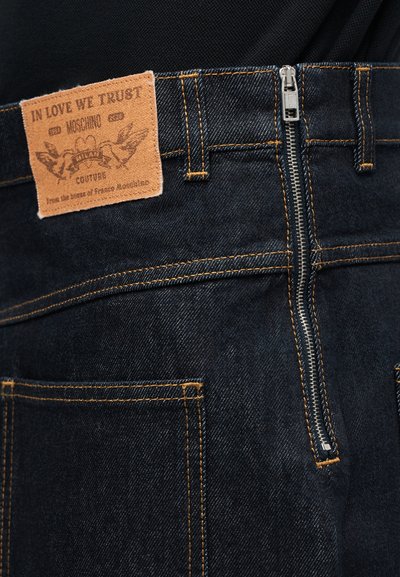 Σκούρο τζιν με κάθετο ασημένιο φερμουάρ στο πίσω μέρος και ταμπελάκι από καφέ δέρμα με την επιγραφή "In Love We Trust Moschino".