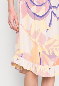 Vestido com padrão floral em cores pastel, apresentando uma bainha com babados e um tecido leve. As cores incluem rosa, amarelo e roxo.