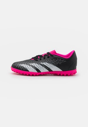 Scarpe sportive in bianco e nero con dettagli rosa, dotate di una parte superiore texturizzata, chiusura con lacci e suola in gomma con tacchetti per migliorare la presa.