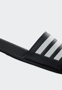 Black slide sandal featuring a textured black strap with three white stripes and a cushioned sole. Simple design with no additional accents.
