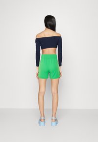 Pantaloni corti verdi con una fascia elastica in vita, abbinati a un top blu navy a spalle scoperte e zoccoli blu con plateau. Design semplice e casual.
