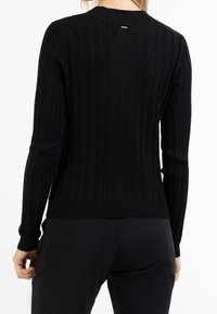 Svart ribbad stickad tröja med långa ärmar, rund halsringning och en figurnära silhuett. Har ett texturerat mönster och en snug midja.