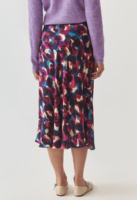 Jupe midi fluide avec un motif abstrait multicolore, mettant en avant des nuances de violet, rose et bleu, fabriquée en tissu lisse avec un léger éclat.