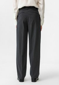 Zwarte pinstripe broek van lichtgewicht stof, met een hoge taille, twee achterzakken en een relaxed fit.