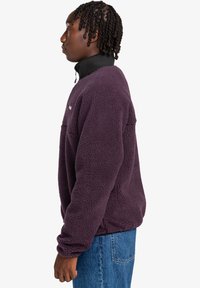 Fleece mikina tmavě fialové barvy, s vysokým límcem a půlzipem vpředu. Měkká, texturovaná tkanina s dlouhými rukávy a volným střihem.