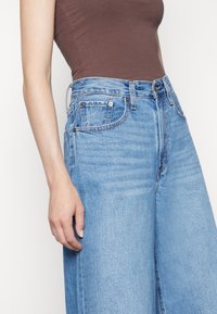 Ljusa blå högmidjade jeans med avslappnad passform, med framfickor, subtil blekning och en standard dragkedja och knappstängning.