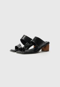 Sandales à talons noirs avec un motif reptile texturé, bout ouvert et un talon en bloc en bois massif. Doublure intérieure en noir lisse.