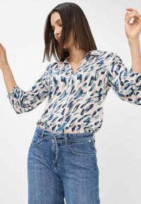 Long-sleeve button-up shirt in a lightweight fabric with a pink and blue abstract pattern, paired with high-waisted, light blue jeans.
