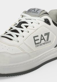 Baskets blanches à lacets avec détails gris et logo EA7 Emporio Armani sur le côté et la languette, avec une semelle en caoutchouc texturée.