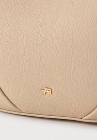 Borsa a mano in pelle beige con superficie testurizzata e dettagli del logo in oro. Forma arrotondata con sottili accenti di cucitura.