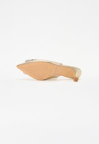 Zapato de tacón alto dorado con puntera afilada, suela texturizada y adornos de strass en la parte delantera. Parte superior de cuero con un tacón delgado.