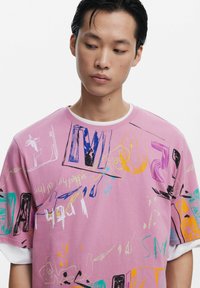 Roze katoenen T-shirt met korte mouwen, voorzien van kleurrijke abstracte schetsen en gedurfde tekstgraphics. Crew neck ontwerp.