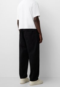 Black denim pants with a loose fit, featuring back pockets and a high waist. Worn with a cropped white t-shirt and beige sneakers.