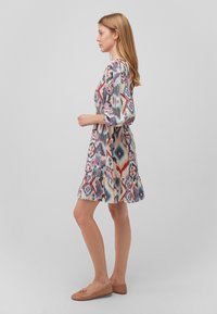Gemustertes Kleid mit lebhaften geometrischen Formen in Rot, Blau und Lila. Leichter Stoff, 3/4-Ärmel und Rüschensaum.
