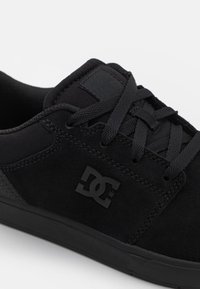 Black skate shoes made of suede and mesh with flat laces, rubber sole, and a prominent black DC logo on the side.
