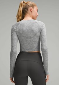 Grauer langer, langärmliger Cropped-Top mit strukturiertem Finish, ausgestattet mit Raglanärmeln und einem figurnahen Design, kombiniert mit hoch taillierten schwarzen Leggings.