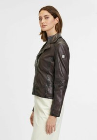 Giacca da moto in pelle marrone con vestibilità strutturata, tasche con zip, dettagli a coste sulle maniche e un badge logo argentato sulla spalla.
