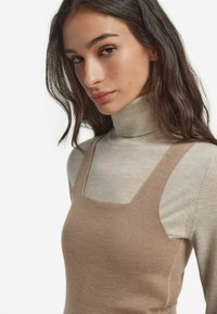 Beżowa kamizelka na jasnoszarym golfie, z kwadratowym dekoltem i miękką fakturą, o dopasowanym kroju i subtelnych szwach.