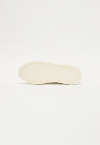 Off-white kaucsuk talp, texturált tapadási mintával és enyhén ívelt orral, rövid oldalsó bordákkal a szélein.