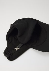Čierna čiapka s mäkkou fleece podšívkou, s nastaviteľným popruhom a kovovou sponou. Exteriér je hladký a šilt je tuhý.