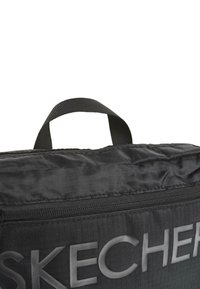 Bolso negro de Skechers con un tejido texturizado, asa superior y gran logo en relieve. Cuenta con un cierre de cremallera y un diseño de patrón en cuadrícula.