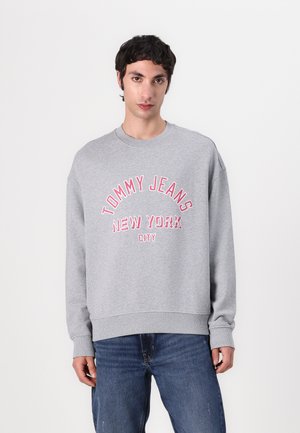 Gray sweatshirt with a crew neck, featuring text "TOMMY JEANS NEW YORK CITY" in pink. Casual fit with ribbed cuffs and waistband.
