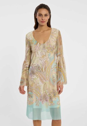 Frau in einem pastellfarbenen Kleid mit Paisley-Muster, langen ausgestellten Ärmeln und einem Rundhalsausschnitt, steht vor einem schlichten weißen Hintergrund.