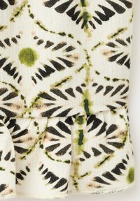 Tissu blanc avec motif floral vert et noir comprenant des formes circulaires et en feuilles et un détail de couture froncée.