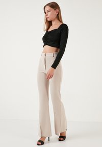 Top corto nero con maniche lunghe e scollatura quadrata, abbinato a pantaloni beige a vita alta svasati con fessure frontali. Sandali neri con tacco.