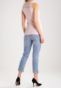 Ljusrosa ärmlös topp med spetsdetaljer på baksidan, kombinerad med uppvikta ljusa jeans och svarta högklackade skor.