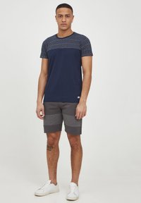 Camiseta azul marino con mangas texturizadas y cuerpo liso, combinada con pantalones cortos grises de diseño en bloques de color y zapatillas blancas.