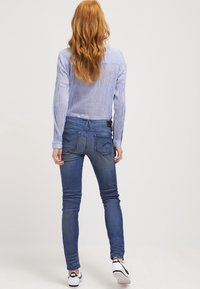 Blauw gestreept overhemd met lange mouwen gecombineerd met nauwsluitende blauwe jeans. De jeans hebben een lichte vervaging en een stikseldetail op de achterzak. Zwart-witte sneakers.