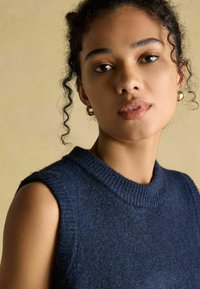 Tumesinine varrukateta kootud top soonikkoes ümara kaelusega, millel on pehme tekstuur ja lõdvestunud istuvus. Sile viimistlus ja minimaalne detailide hulk.