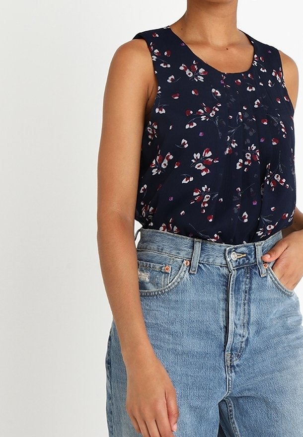 Mörkblå ärmlös blus med blommönster i rött och vitt, med en plisserad front och lättviktig tyg, kombinerad med högmidjade jeans.