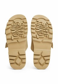Suelas de goma de color marrón con surcos profundos, con "TOMMY JEANS" grabado en el centro. Textura ligera con forma plana y bordes redondeados.