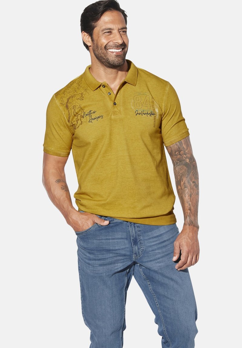 Yellow polo shirt with short sleeves, three-button placket, and printed accents on the front, paired with light blue jeans.