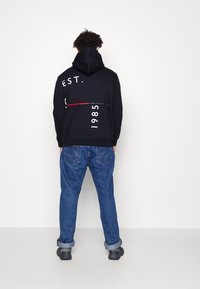 Black hoodie with white text and red accents, paired with blue denim jeans. The pants have rolled cuffs and a relaxed fit.