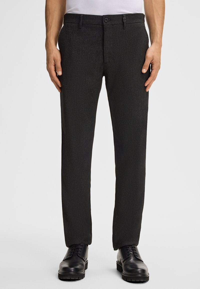Pantaloni formali neri con un motivo testurizzato, vestibilità sartoriale, davanti piatto, passanti per cintura e tasche laterali, abbinati a scarpe eleganti nere.