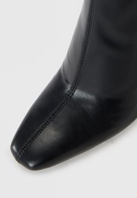 Black leather ankle boot with a pointed toe, smooth texture, and visible stitching along the seams, showcasing a sleek silhouette.