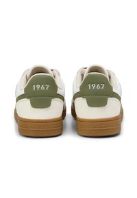 Bílé tenisky s zelenými akcenty, texturovanými gumovými podrážkami a reliéfním detailem "1967" na patě. Měkký materiál a zakulacený tvar.